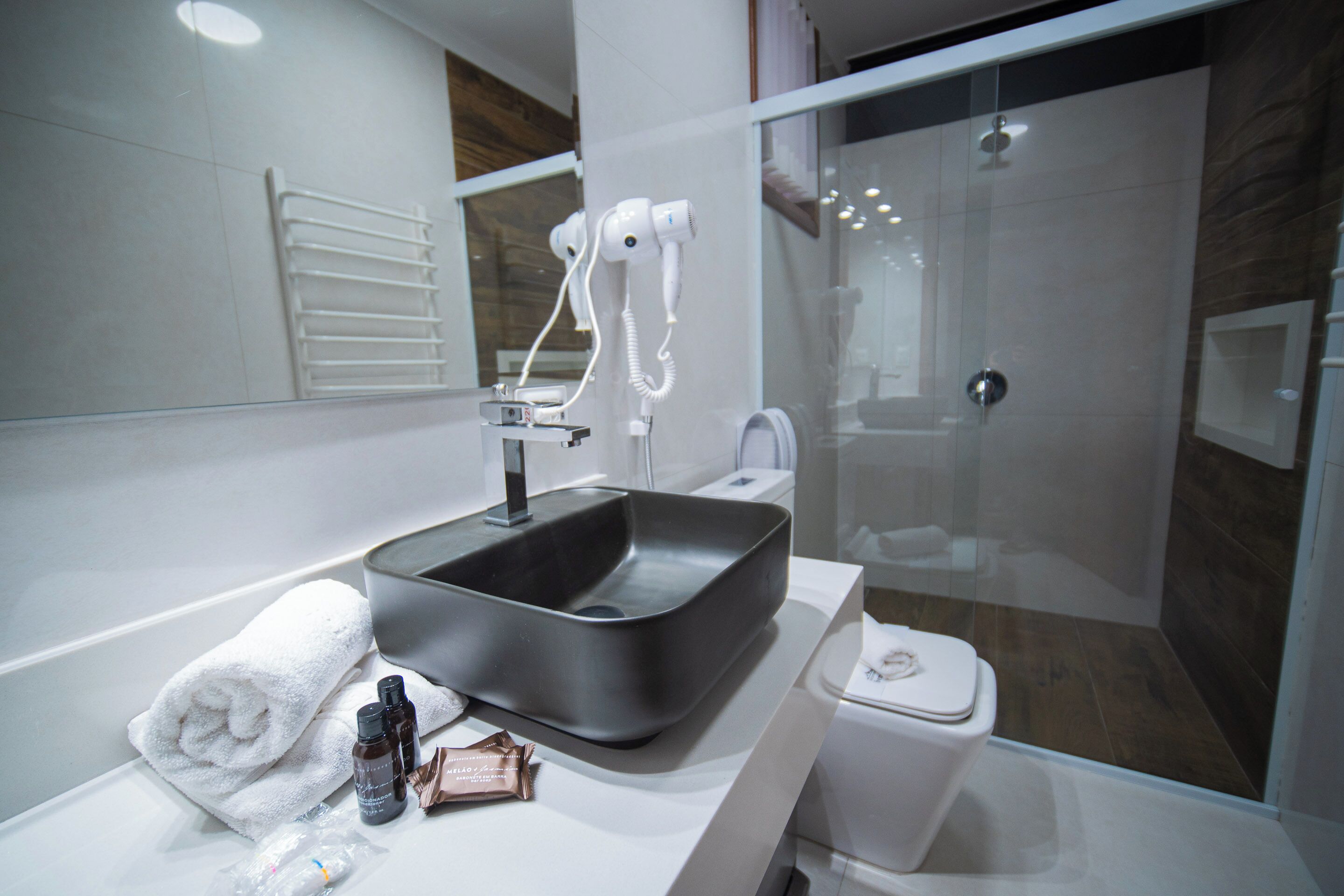 Uma casa de banho moderna com lavatório preto, toalha branca e cabine de duche em vidro.
