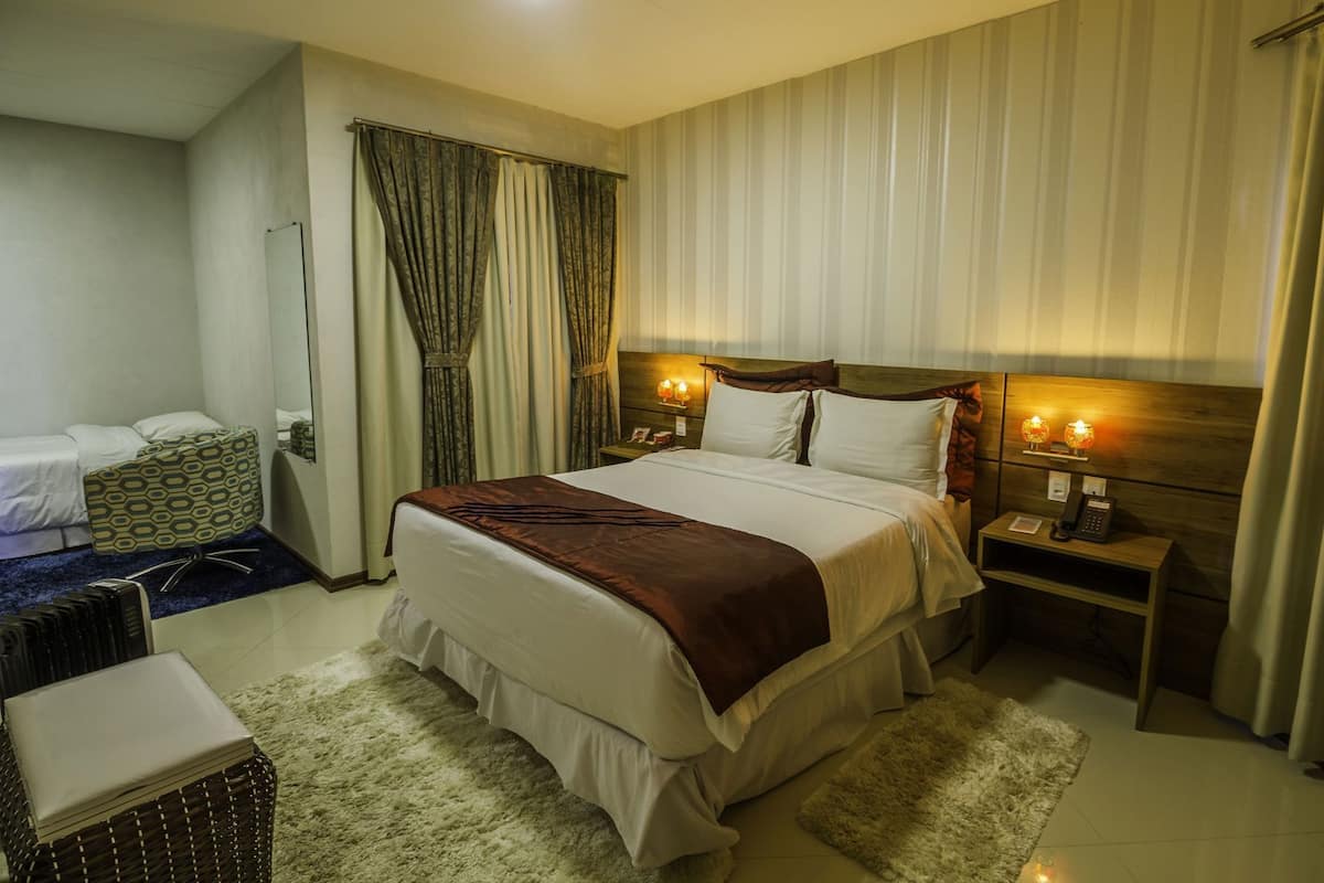 A hotel room with a bed, bedside tables, a chair, and a small table with a lamp.