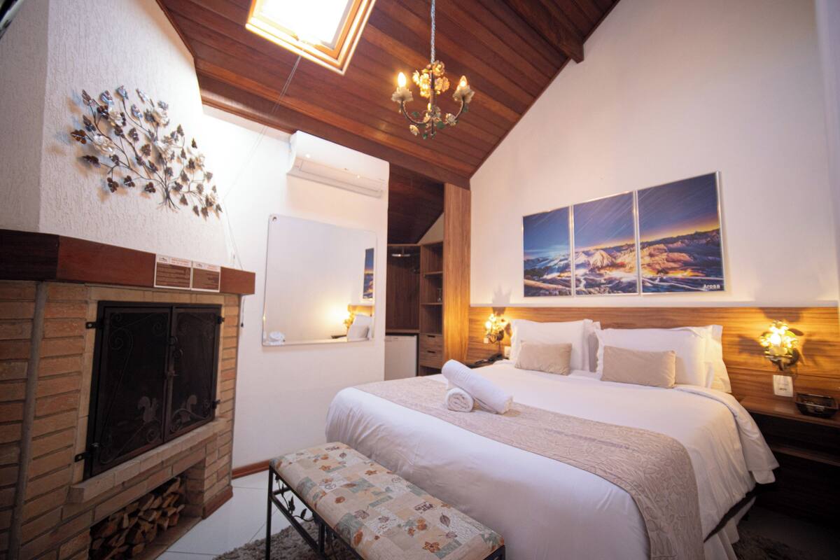 A bedroom with a fireplace, a bed, a bench, and a large landscape painting.