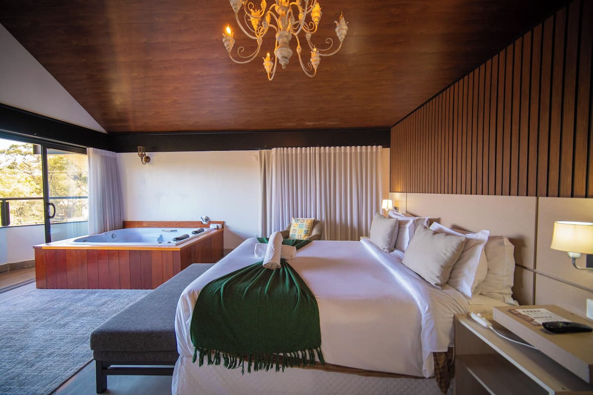 A hotel room with a large bed, a separate seating area with a hot tub, a chandelier, and a view of the outdoors.