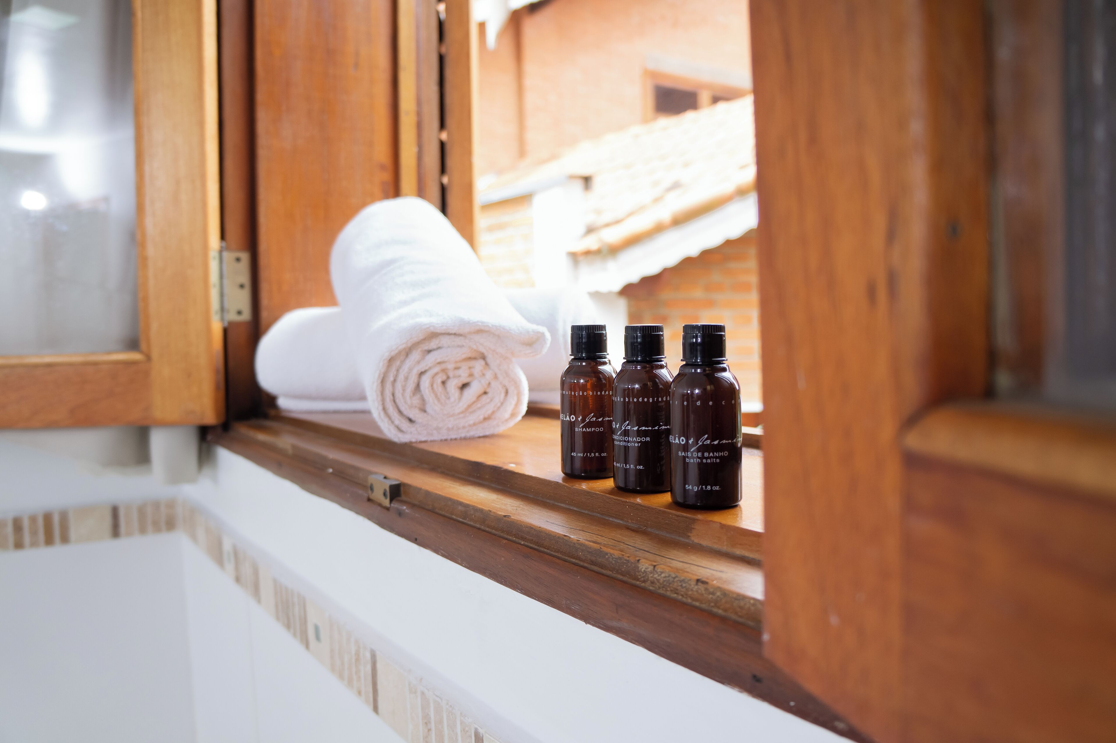A window view with a towel and three bottles of shampoo on a wooden ledge.