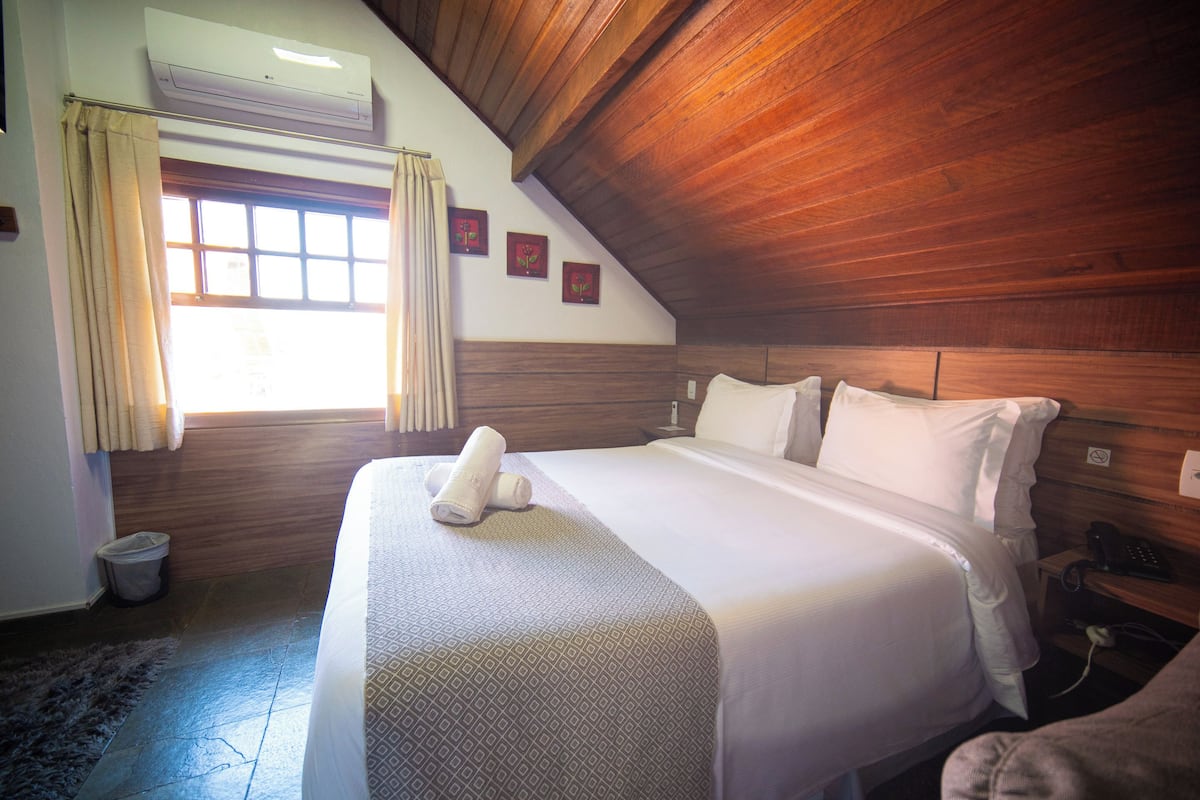 A hotel room with a large bed, wooden ceiling, and a window with curtains.