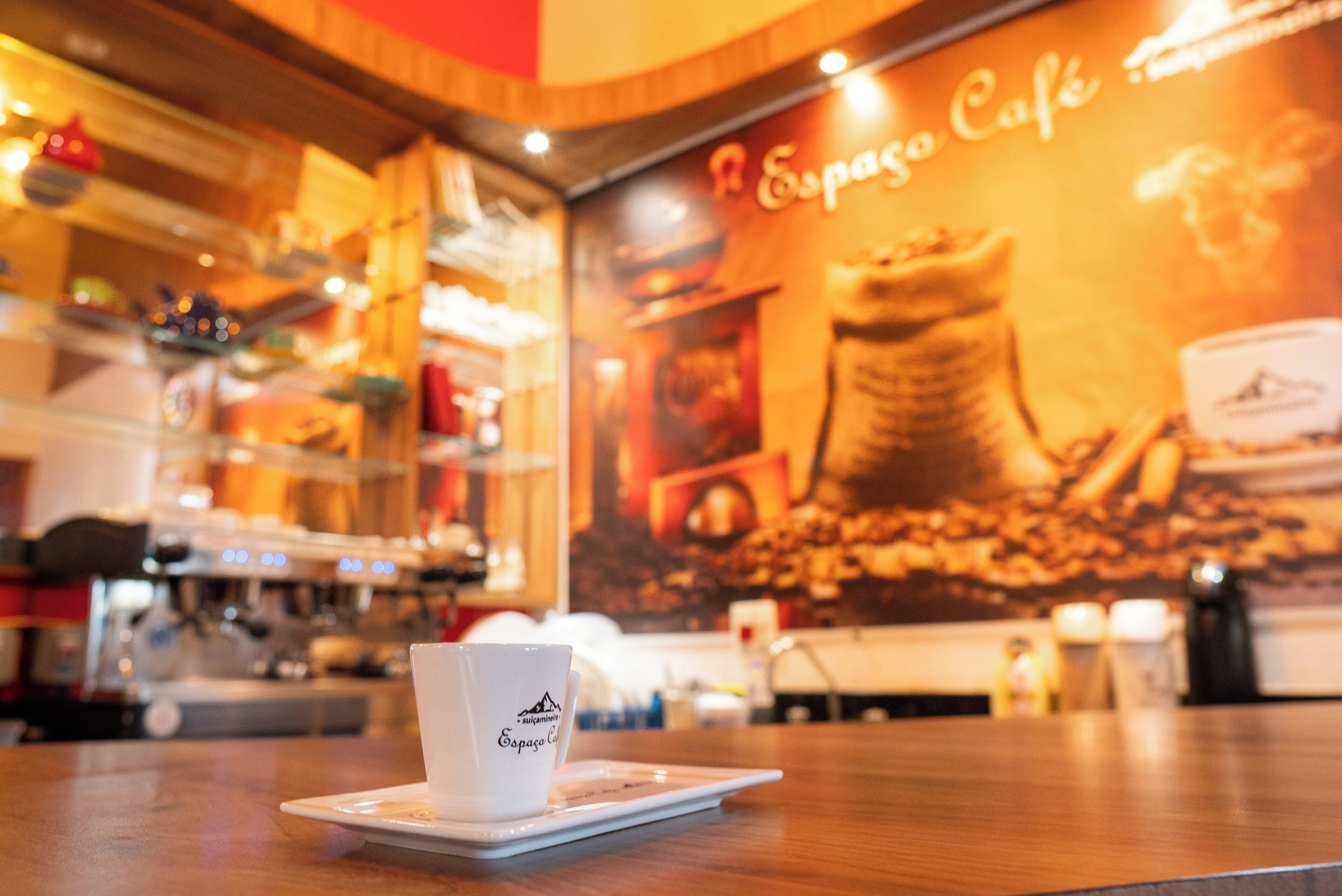 A coffee cup on a tray in a cafe with a large espresso-themed mural in the background.