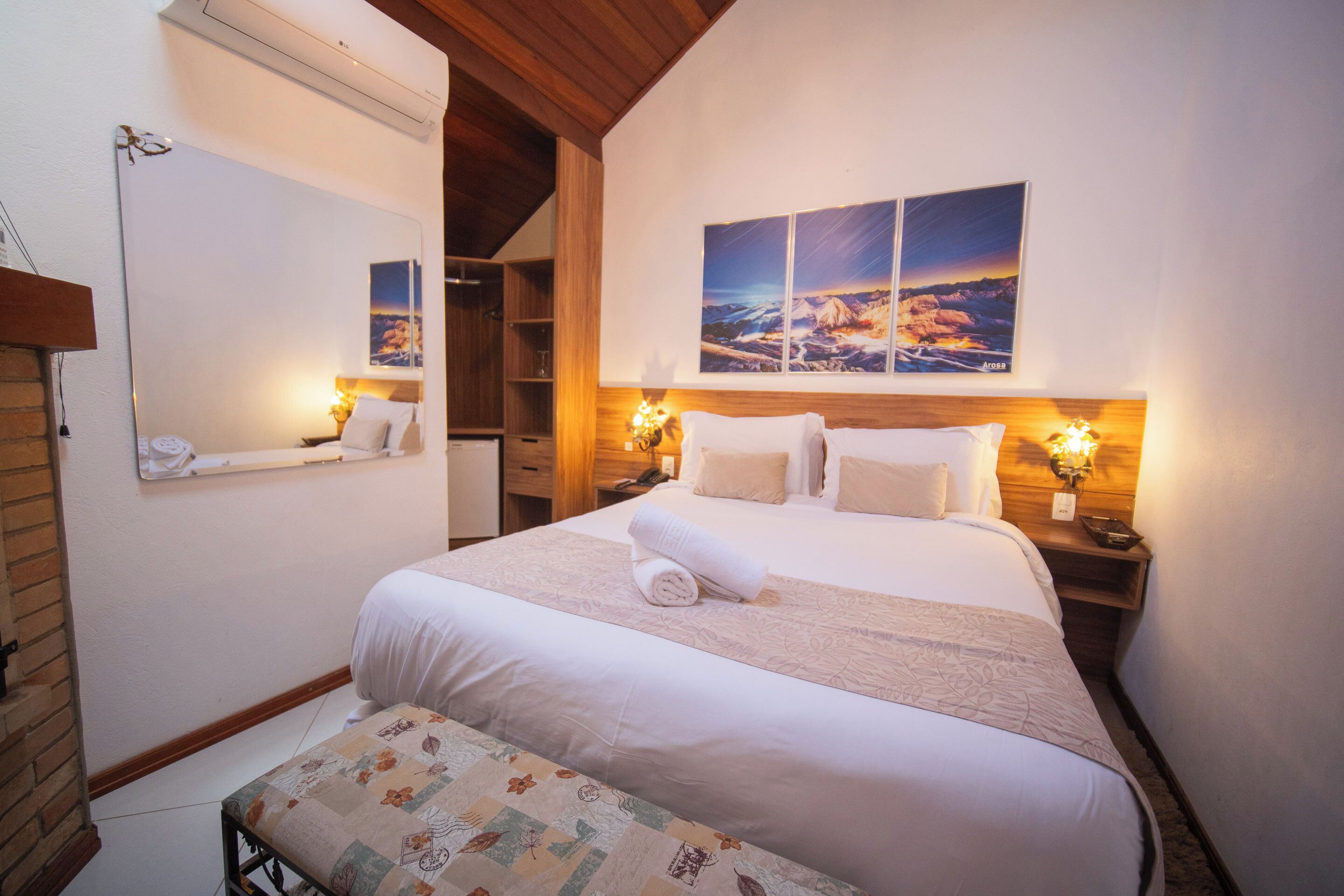 Habitación de hotel con una cama grande, techo de madera, televisor montado en la pared y un cuadro sobre la cama.