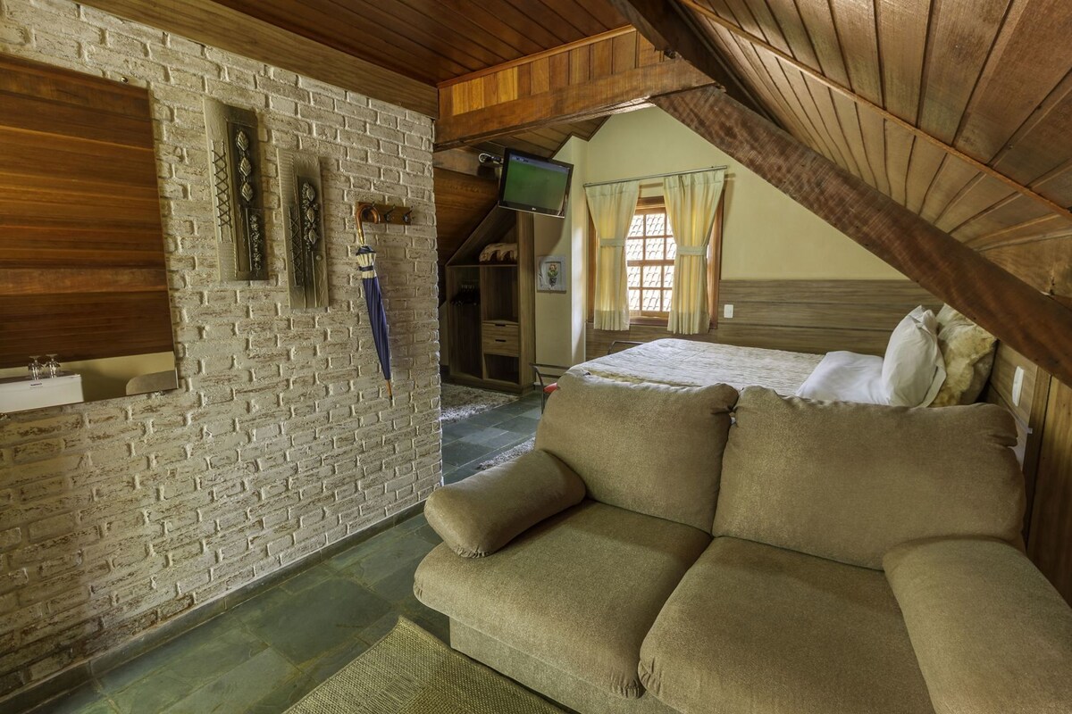 A cozy room with a brick wall, a wooden ceiling, a sofa, a television, and a bed.