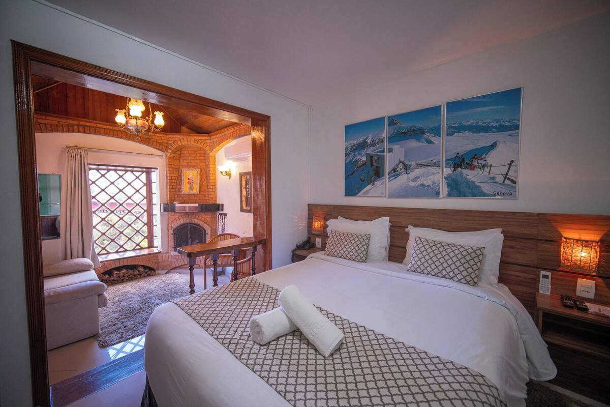 A hotel room with a large bed, a fireplace, a dining table, and a view of the mountains.