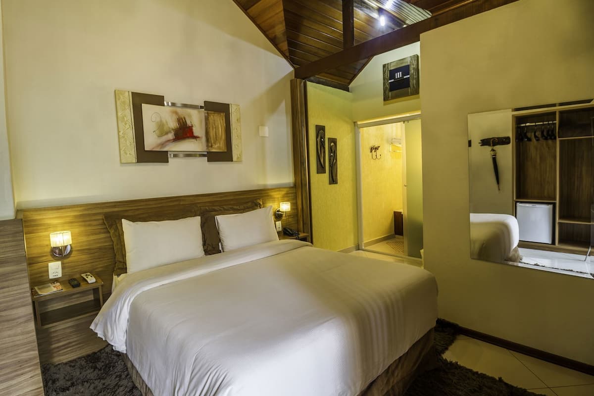 A hotel room with a large bed, bedside lamps, a mirror, and a wooden ceiling.
