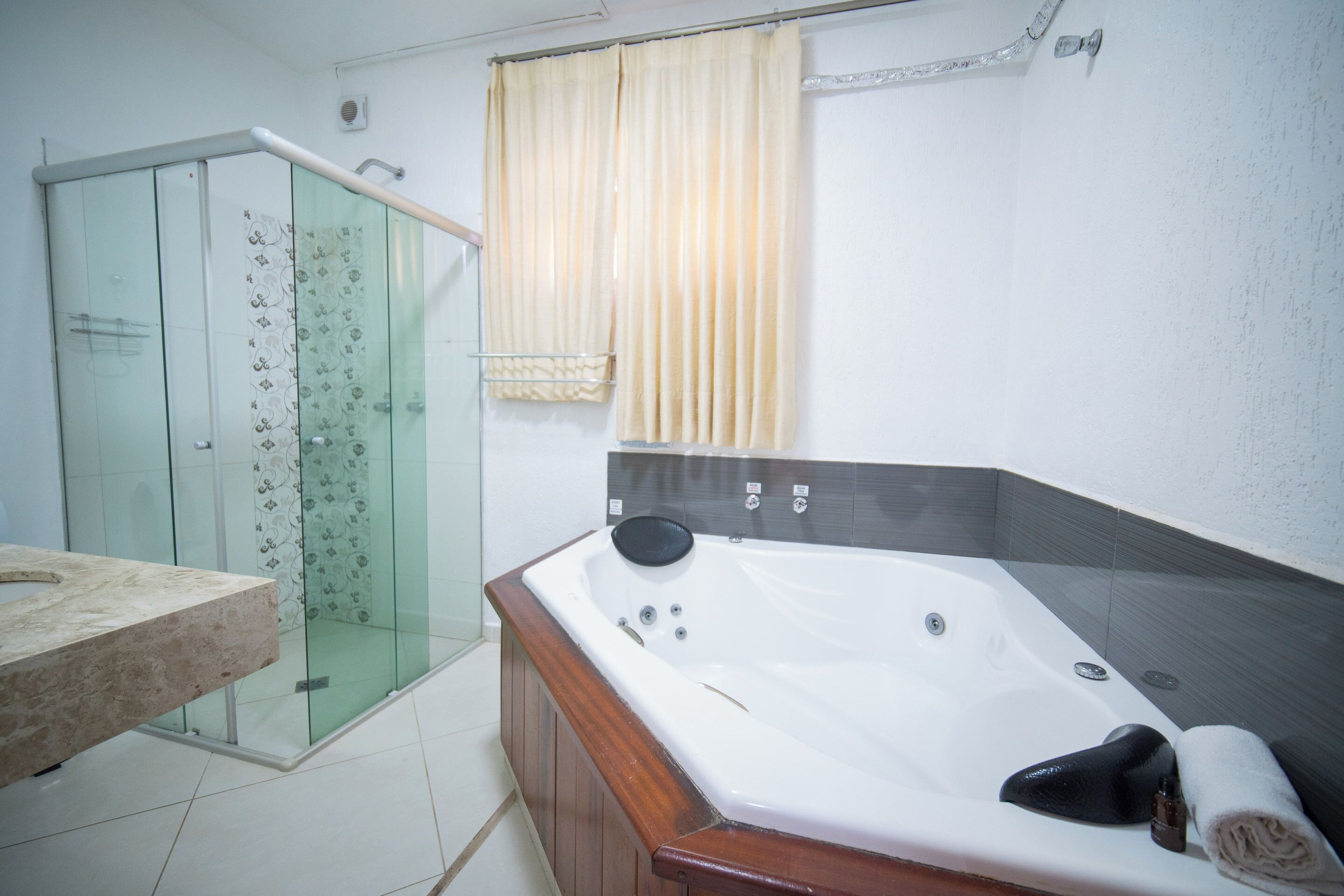 A bathroom with a glass shower enclosure, a wooden vanity, and a large bathtub with a towel and a bottle.