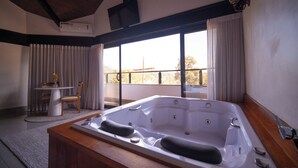 Une salle de bain moderne avec une grande baignoire, une petite table avec des chaises et une vue sur l’extérieur grâce à de grandes fenêtres.