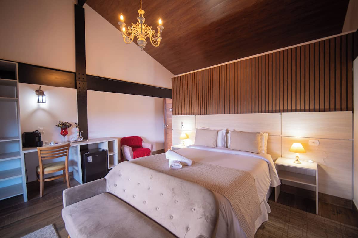A modern hotel room with a large bed, a desk with a computer, a red chair, and a chandelier.
