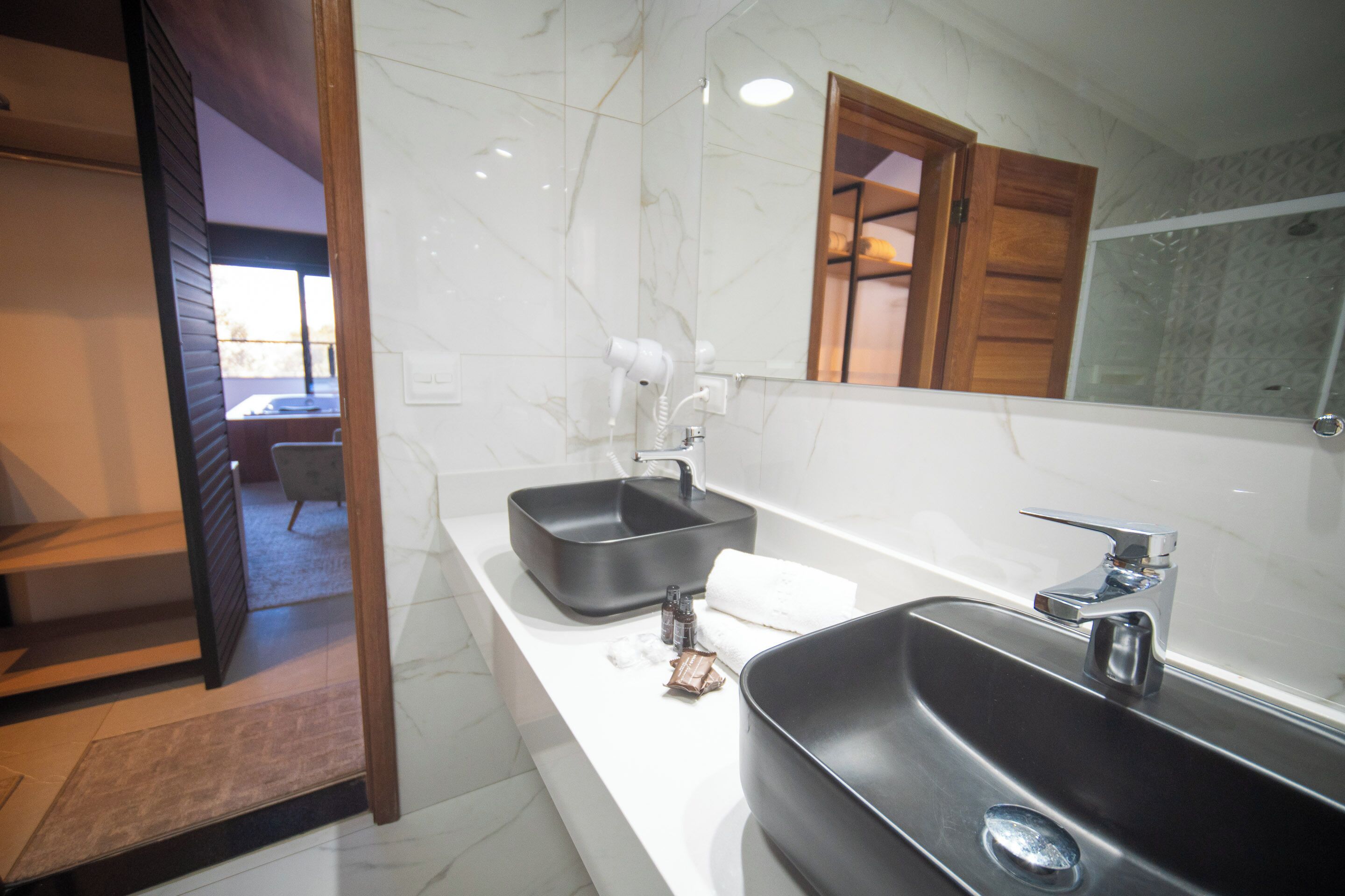 A modern bathroom with a large mirror, two sinks, and a shower.