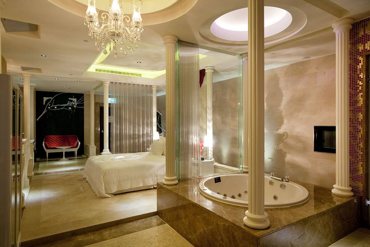 Een luxe slaapkamer met een groot bed, een zithoek en een badkamer met een badkuip en een grote spiegel.