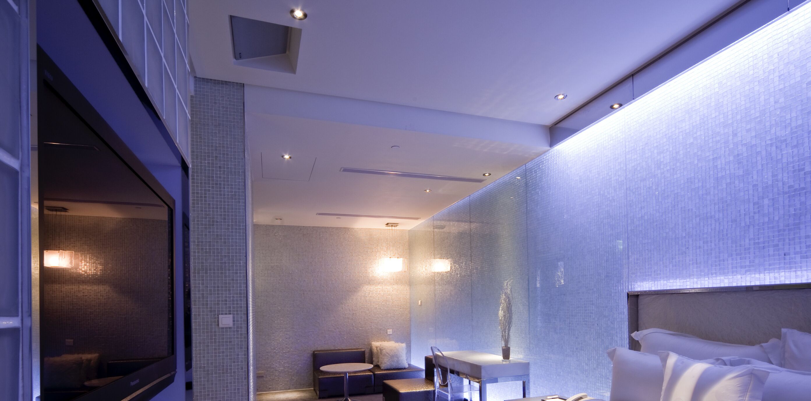 Ein modernes Badezimmer mit Glasabtrennung, einem runden Waschbecken, einem kleinen Tisch und einem Bett mit weißer Bettwäsche.