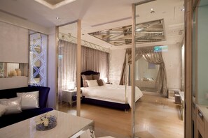 Een moderne hotelkamer met een groot bed, een sofa, een glazen scheidingswand en een zichtbare badkamer door de wand.