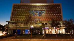 Um edifício moderno com uma placa 'Wee' em destaque, rodeado por árvores e iluminado por postes de luz.
