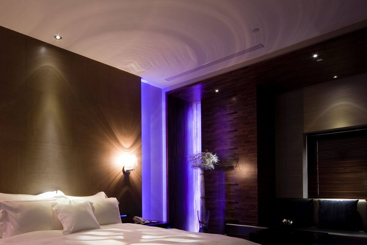 Een moderne hotelkamer met een groot bed, twee wandlampen en een klein tafeltje met een lamp.