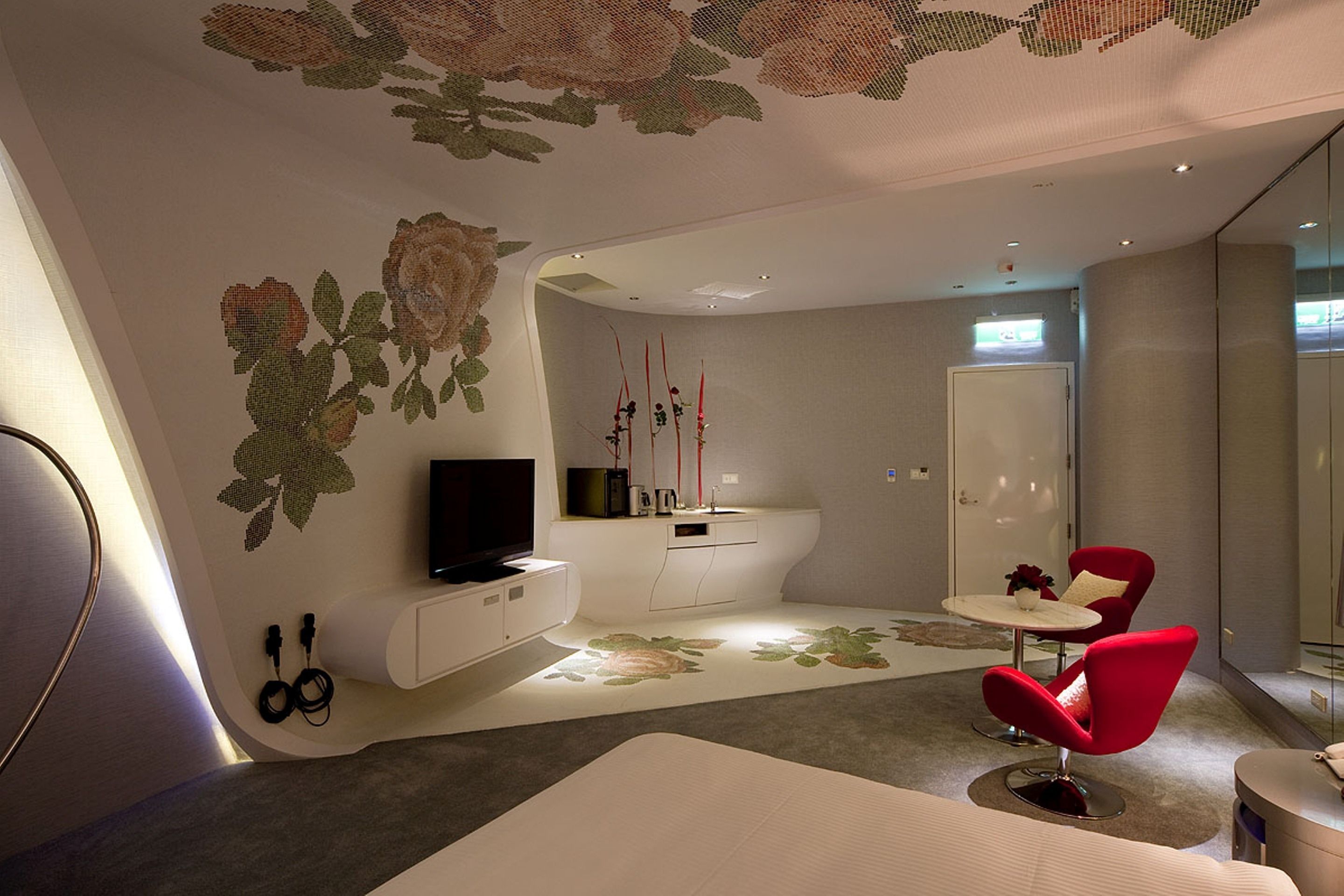 A modern living room with a flat-screen TV, a white sofa, a red chair, and a small round table.