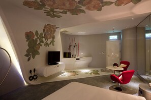 Een moderne woonkamer met een flatscreen televisie, een witte bank, een rode fauteuil en een kleine ronde tafel.