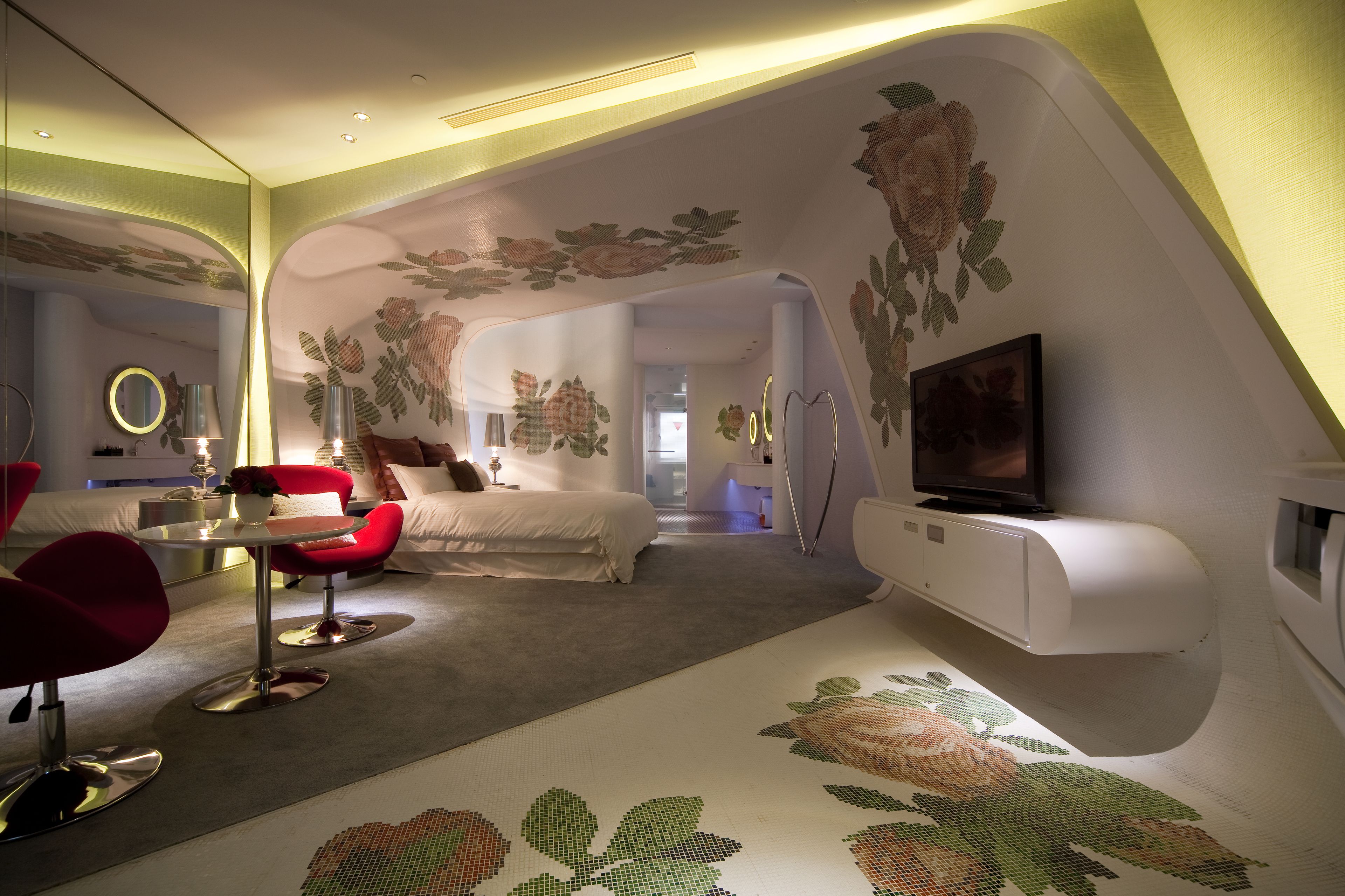 Ein modernes Hotelzimmer mit gewölbter Decke, floralen Wandbildern, einem Bett, einem Fernseher und einem roten Sessel.