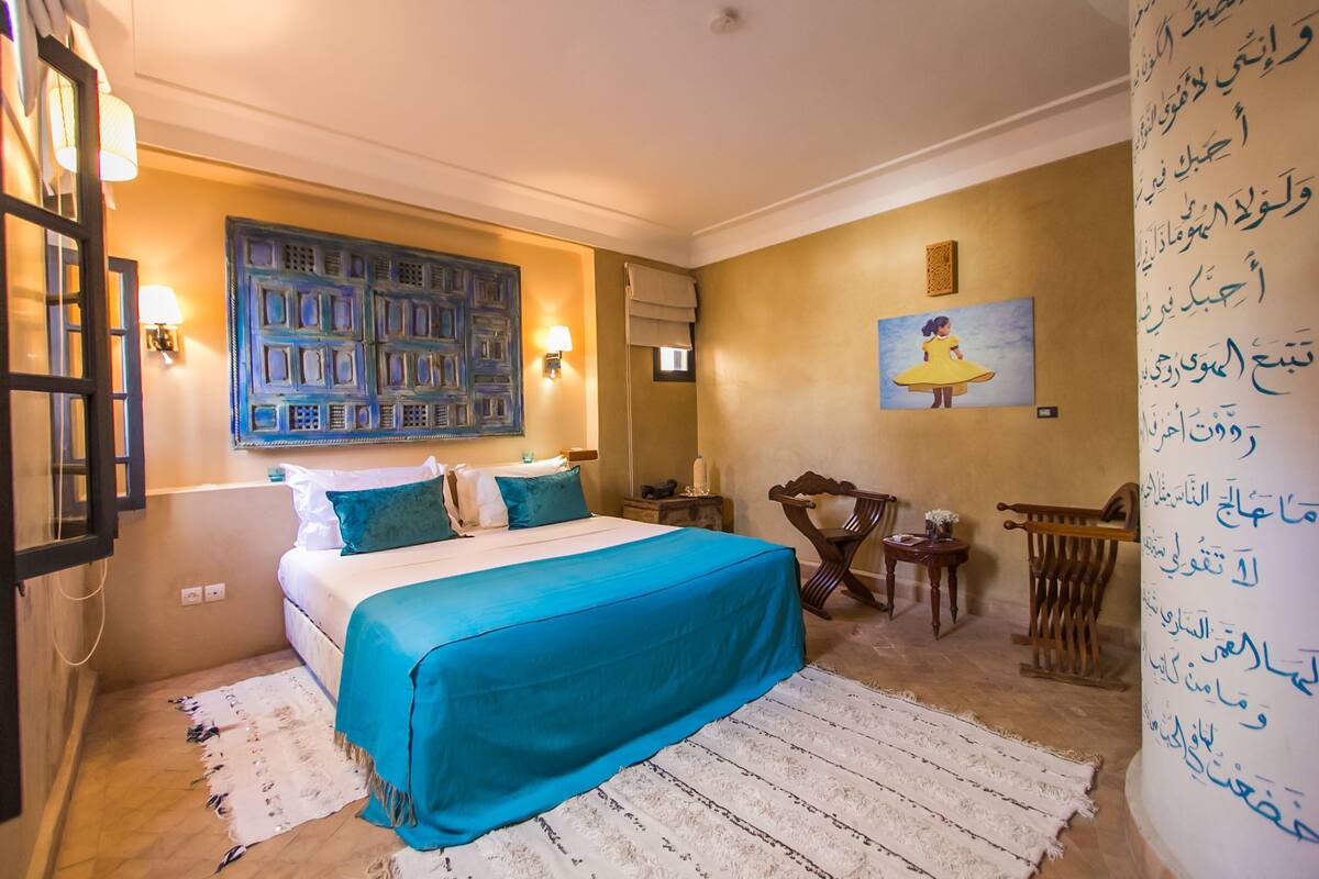 A bedroom with a bed, a painting, a chair, and a wall with writing.