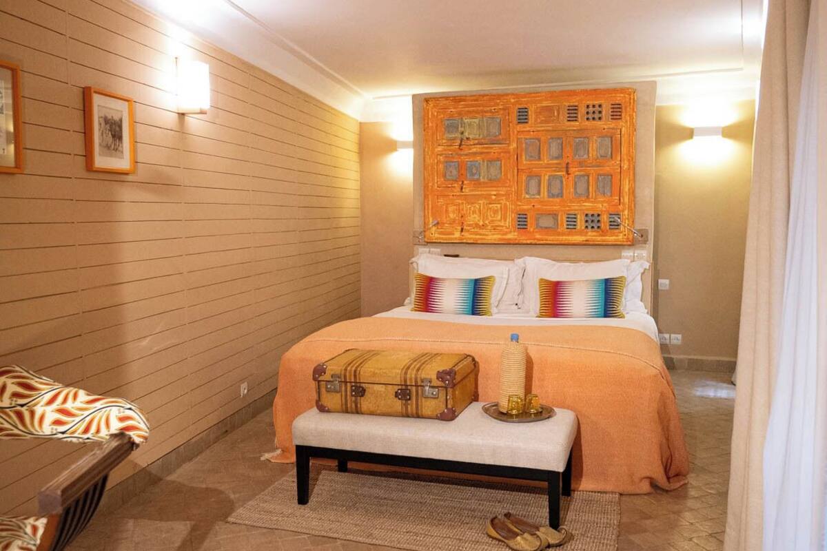 A hotel room with a bed, a bench, a suitcase, and a wall-mounted decorative panel.