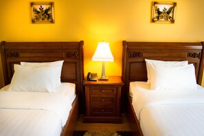 Une chambre d’hôtel avec deux lits, une table de chevet avec une lampe et deux tableaux représentant des motifs floraux accrochés au mur.