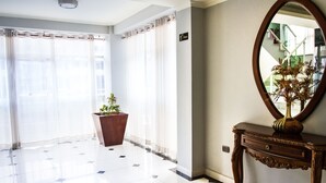 Un vestíbulo de hotel con suelo de baldosas, una planta en maceta, una consola con un jarrón y un espejo grande.