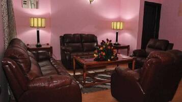 Una sala de estar con un sofá de cuero marrón, una mesa de centro de madera con un centro de mesa floral y dos lámparas de pie.