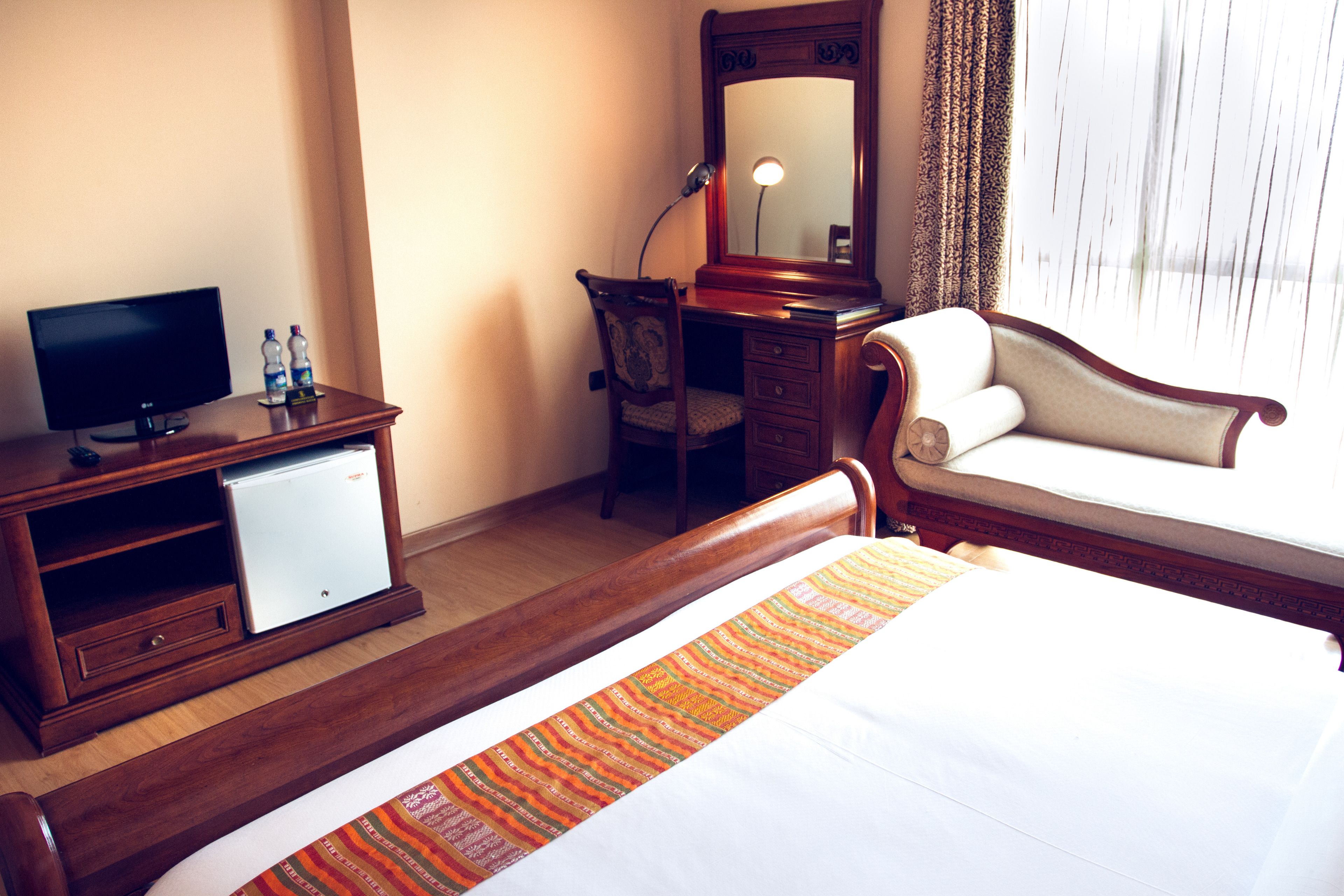 A hotel room with a bed, a desk with a television, a small refrigerator, and a chair.
