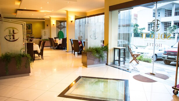 Un hall de hotel con una recepción, zona de estar y grandes ventanales con vistas a la calle.