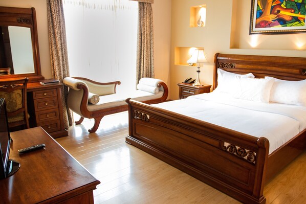 Une chambre d’hôtel avec un lit en bois, un bureau, une chaise et une table de chevet avec une lampe.