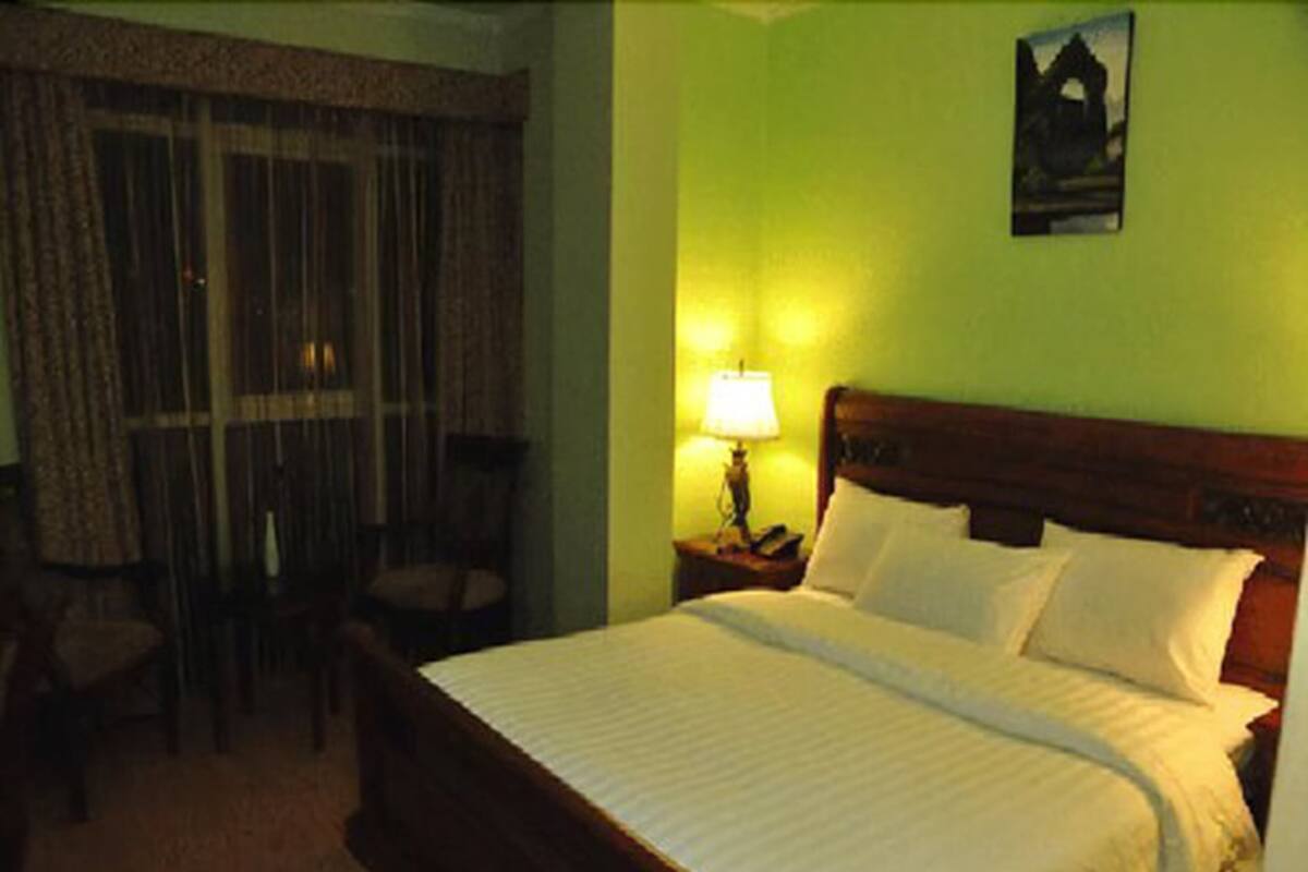 A hotel room with a bed, a nightstand with a lamp, a chair, and a window with curtains.