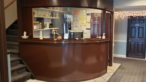 A reception desk with a mirror, a wooden counter, and a staircase to the left. - Jones Beach Hotel (Wantagh)