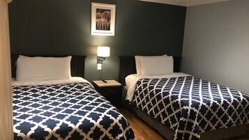 A hotel room with two beds, each with a patterned bedspread, a bedside table with a lamp, and a framed picture on the wall.