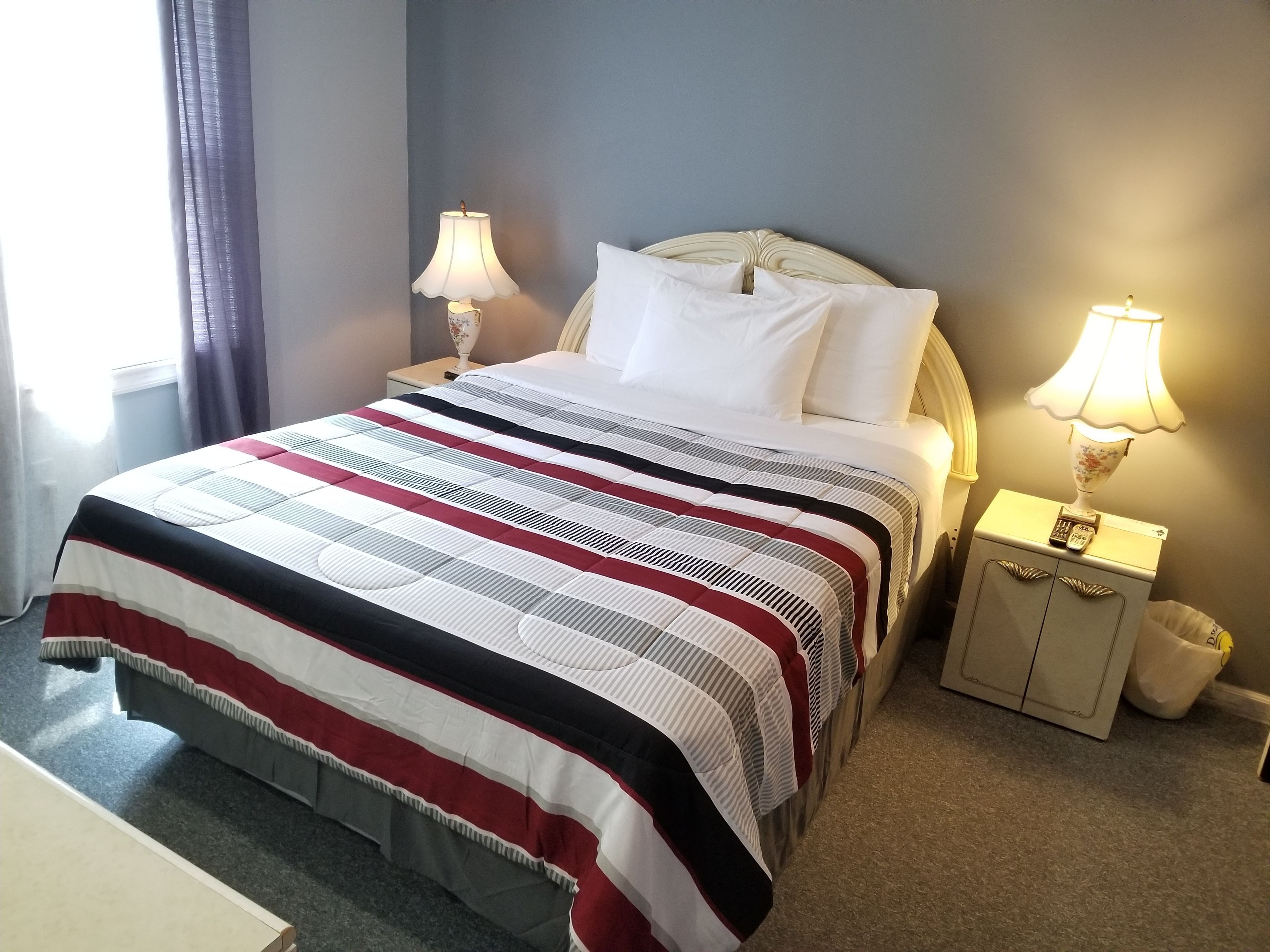 A neatly made bed with a striped bedspread, two bedside lamps, and a nightstand with a remote control.