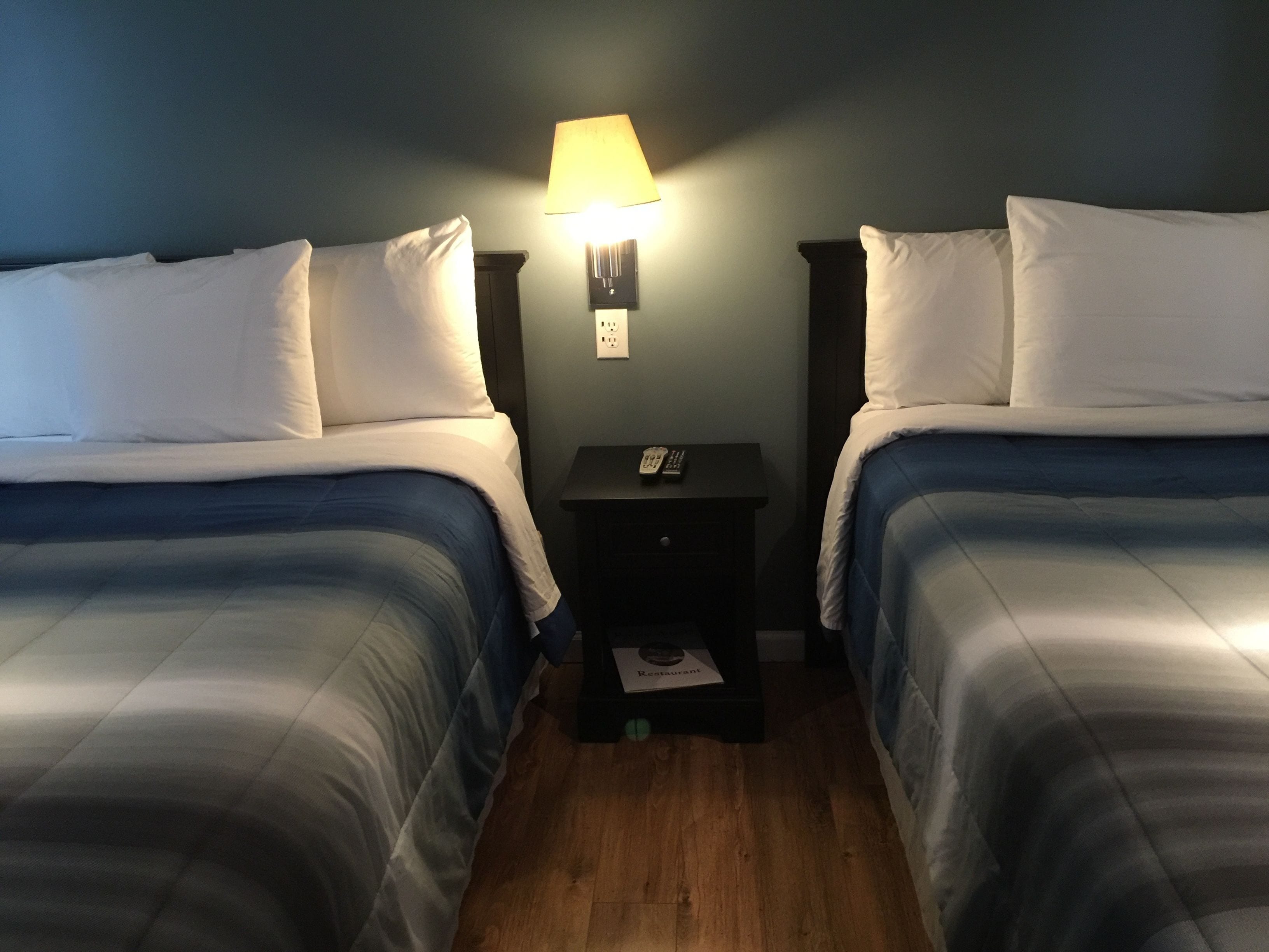 A hotel room with two beds, a nightstand with a lamp, and a small table with a menu.