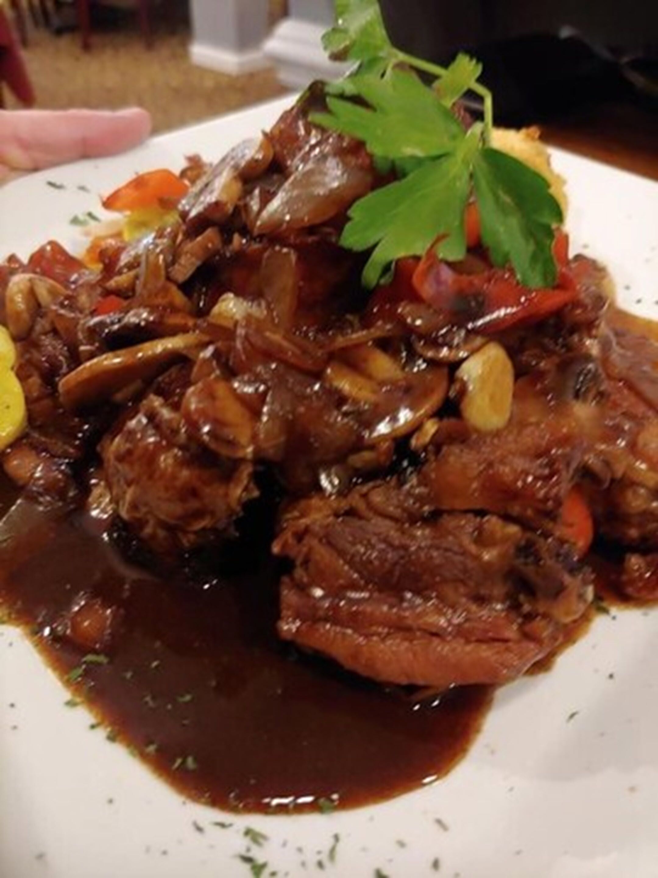 A plate of braised beef with vegetables and a garnish of parsley.