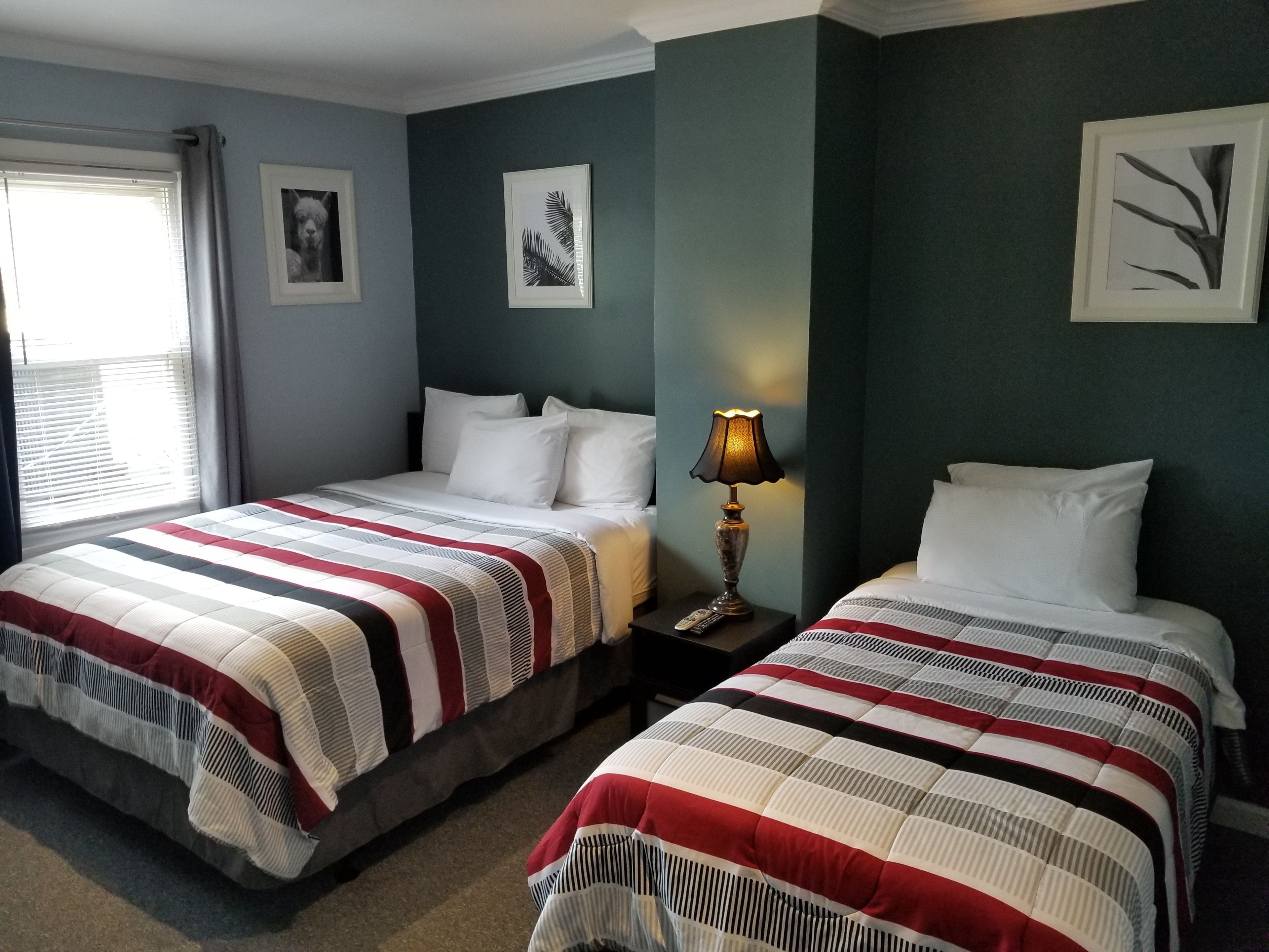 A hotel room with two beds, a nightstand, a lamp, and framed pictures on the walls.