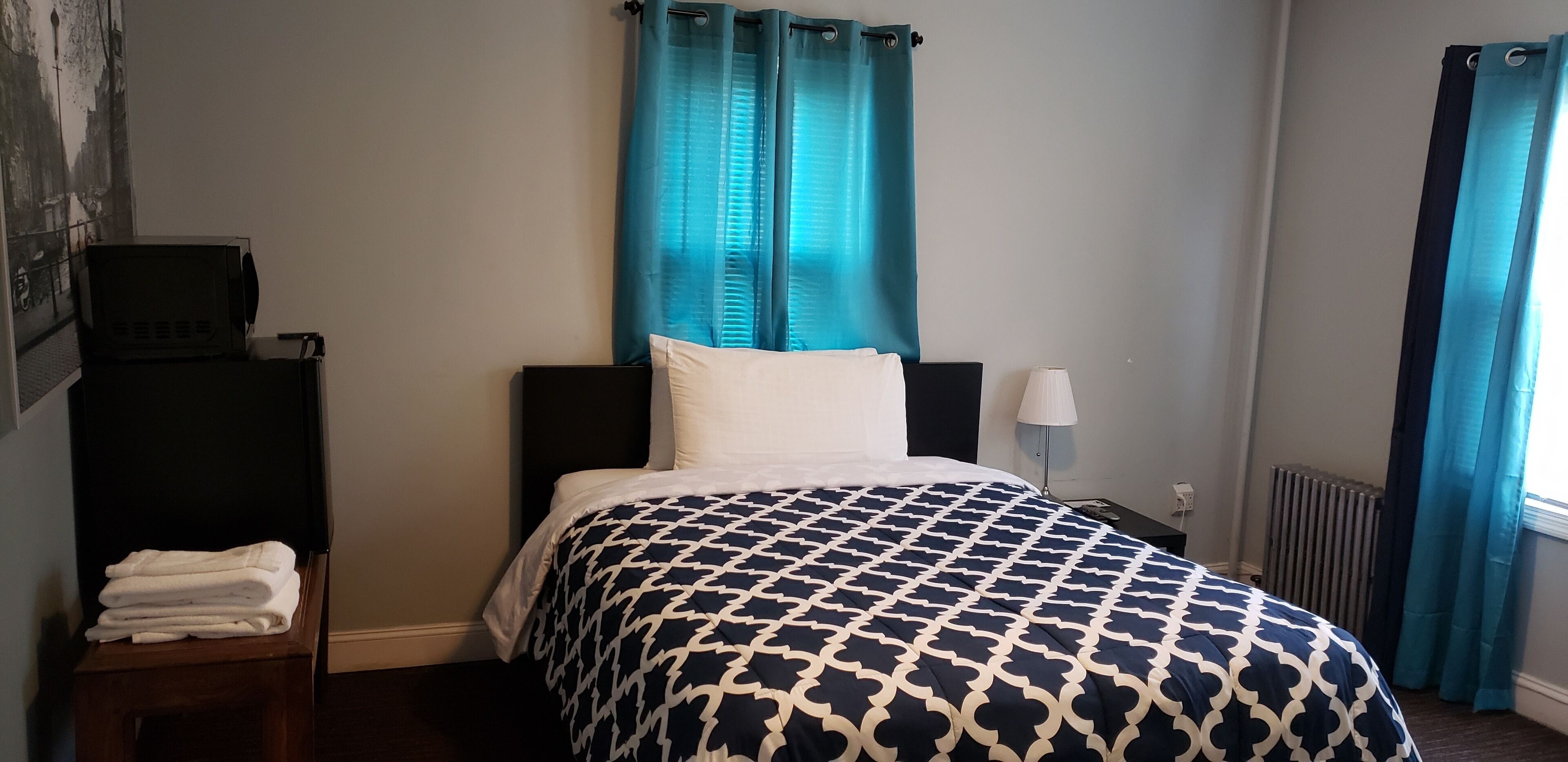 Une chambre d’hôtel avec un lit, une table de chevet, une lampe et un radiateur.