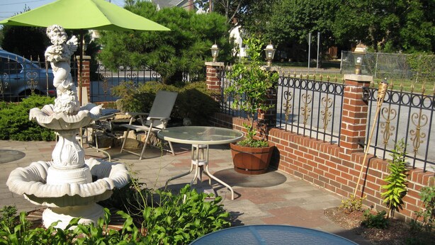 A patio area with a stone fountain, a glass table, and a brick wall. - Jones Beach Hotel (Wantagh)
