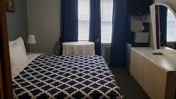 Een hotelkamer met een bed, een klein rond tafeltje, een dressoir en een raam met gordijnen.