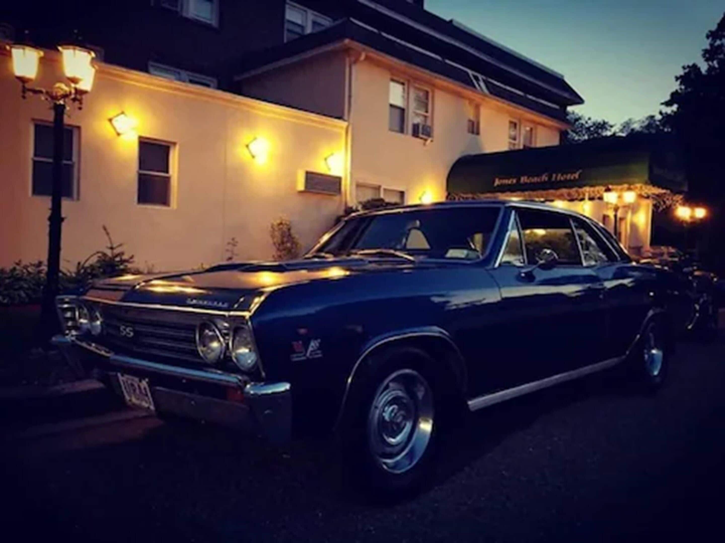 Une voiture noire classique est garée devant un immeuble sur lequel on peut lire l’inscription « Hôtel James Hook ».