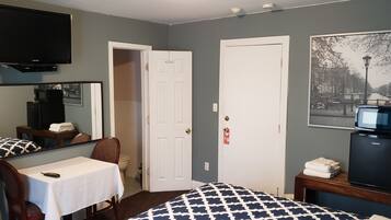 A hotel room with a bed, a desk with a chair, a television, a microwave, a refrigerator, and a door.