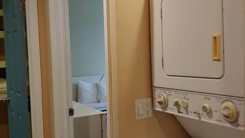 Une buanderie équipée d’un lave-linge et d’un sèche-linge à chargement frontal, une porte donnant sur une chambre et un interrupteur sur le mur.