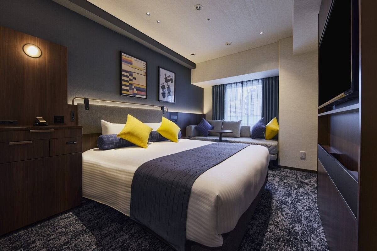 A modern hotel room with a large bed, a desk, a sofa, and a TV.