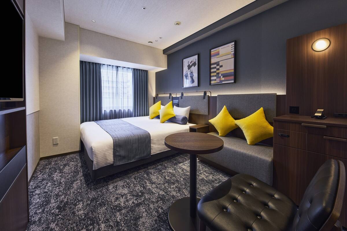 A modern hotel room with a large bed, a sofa, a small table, and a TV.
