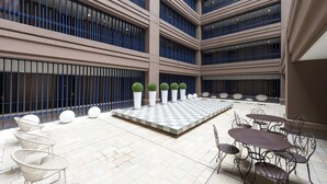 Un amplio patio interior con varios niveles de balcones, zonas de estar con mesas y sillas, y macetas esféricas decorativas.