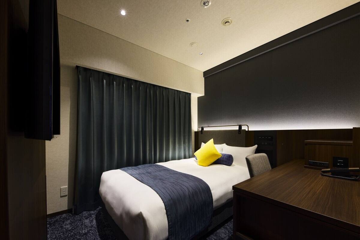 A hotel room with a bed, a desk, a chair, and a television.