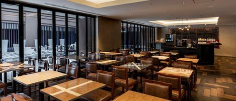 Un interior de restaurante moderno con varias mesas y sillas, una zona de bar y amplios ventanales que ofrecen vistas.