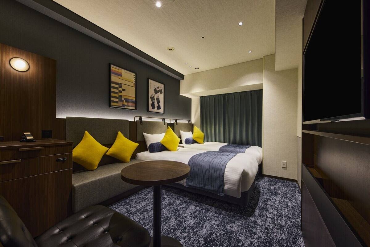 A hotel room with a bed, a desk, a chair, a small table, and a TV.